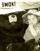 Smokey Bear holding a toddler in a sun hat